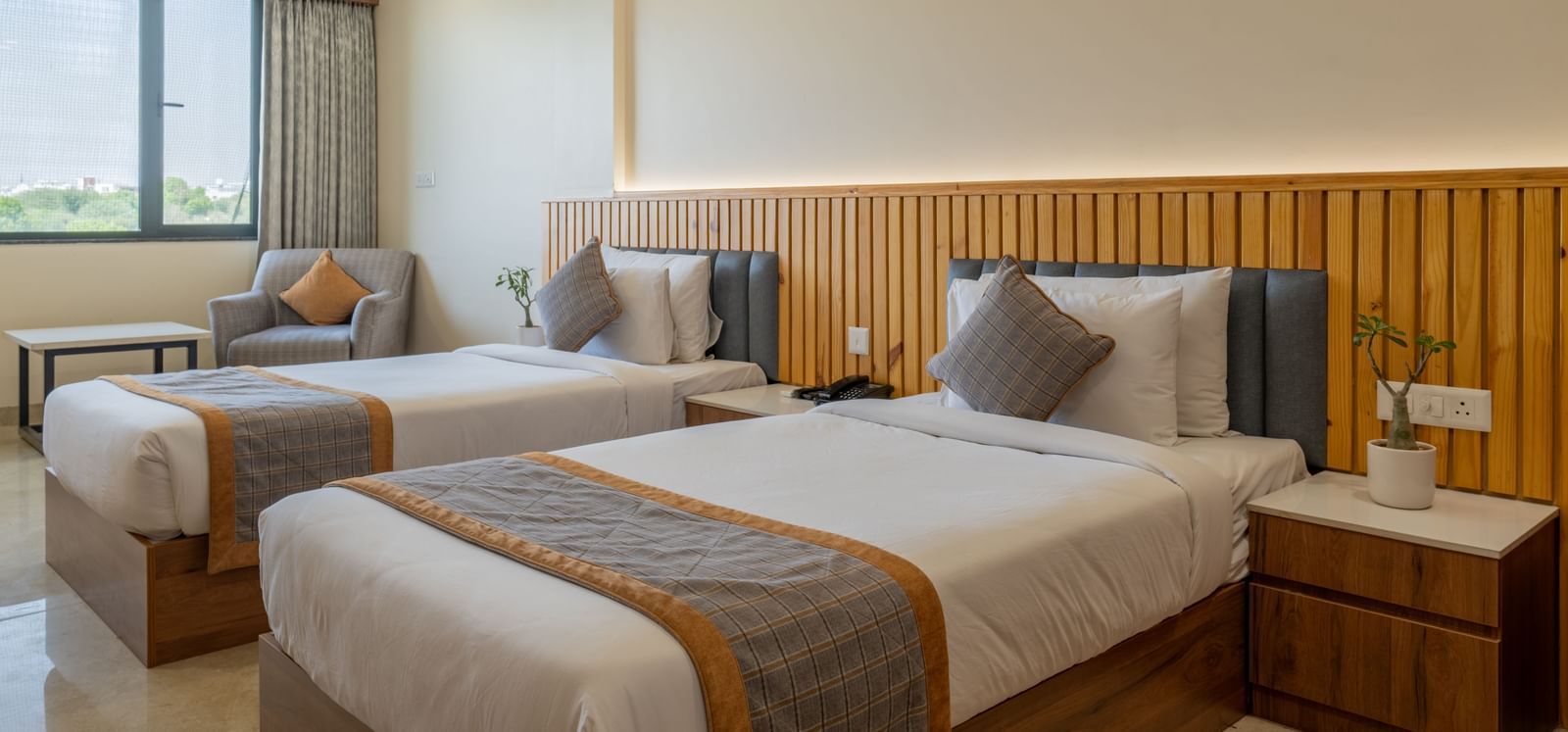 Twin bedroom at Hotel Highway King, Bagru, with bedside tables, large window, and upholstered headboards.