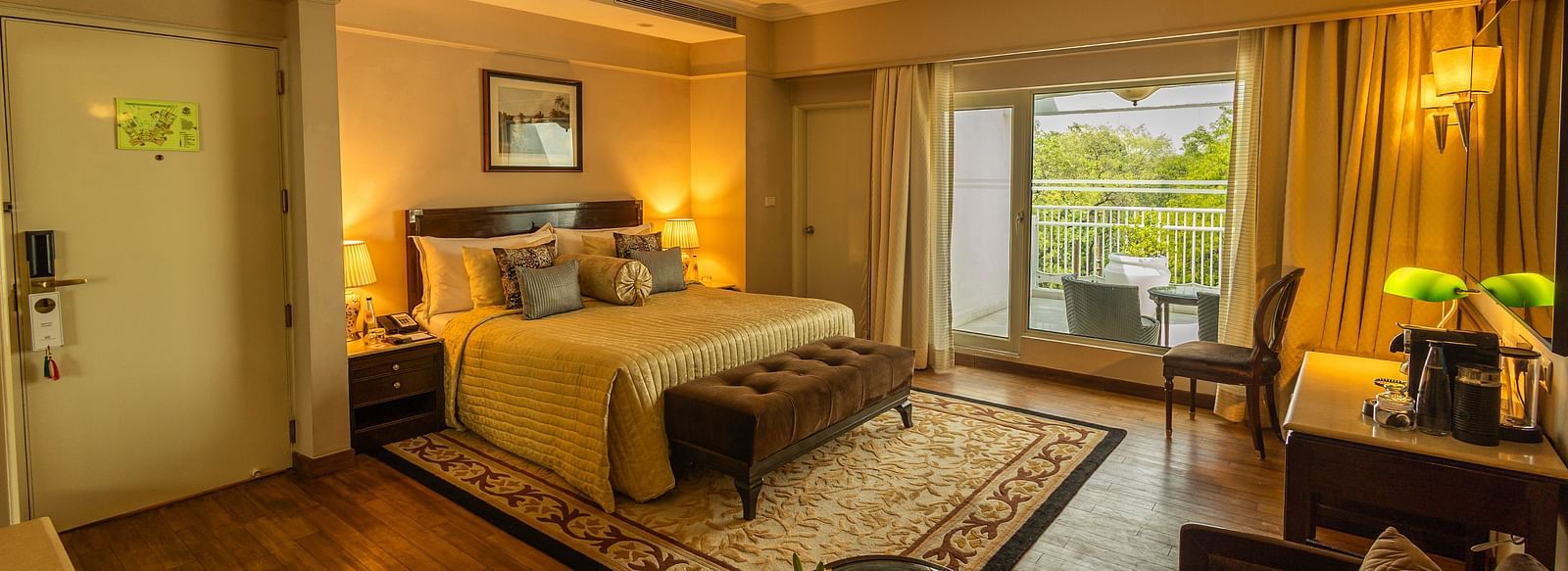 Luxury King Bed Room with Balcony at The Claridges New Delhi, featuring a cosy bed, a framed artwork on the wall, and a glass door to the balcony