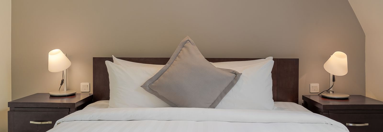 A cosy bedroom with a white bed, bedside tables, and lamps under a sloped ceiling | Four-bedroom Suite | Central Mansions, Phnom Penh