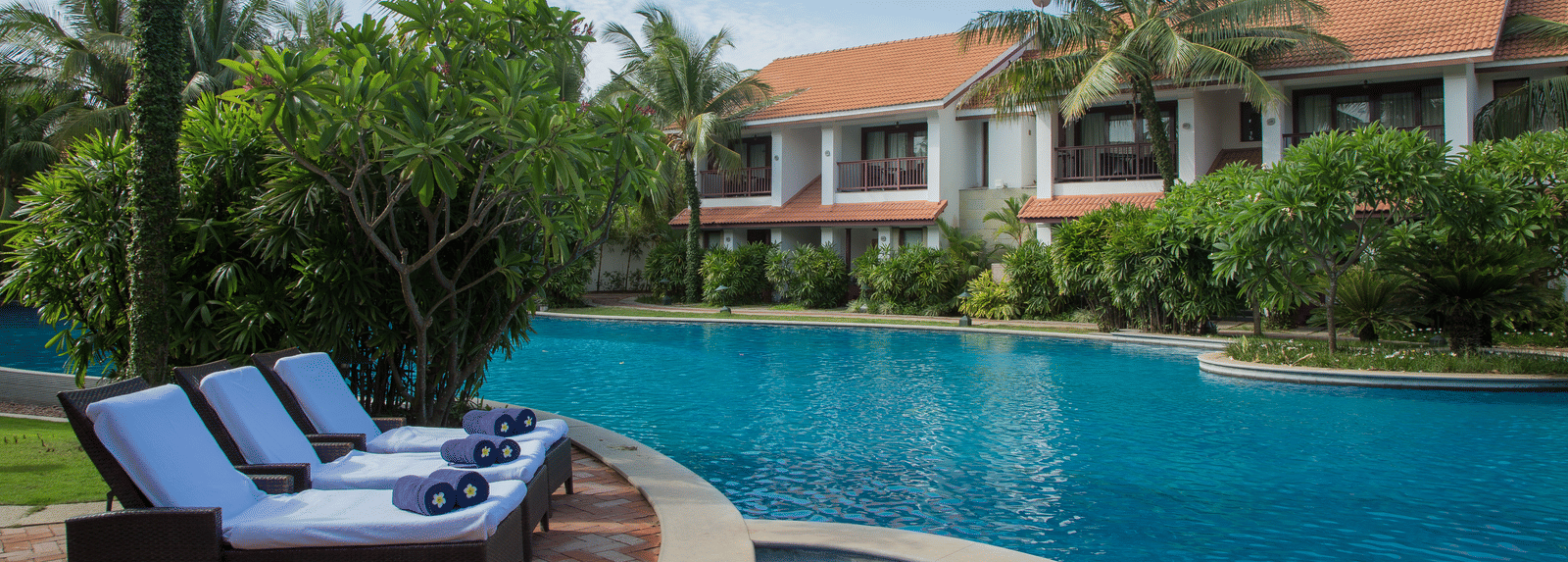 Luxury resort with a swimming pool, lounge chairs, and tropical greenery at GRT Hotels.
