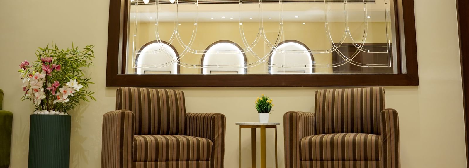A close-up shot of two brown coloured arm chairs placed in the lobby of M2 Square by Monday Premium with a huge mirror above it.