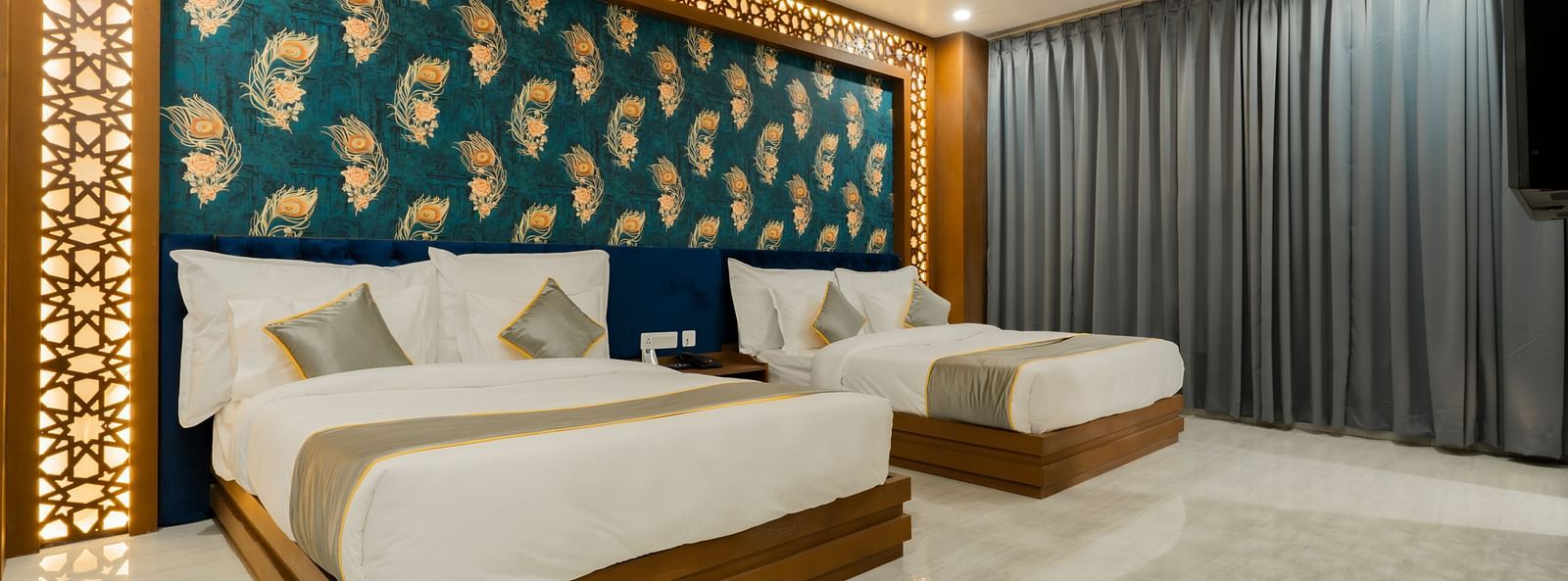 A bedroom at the Bamboo Saa Mulberry Resort featuring two twin beds with white linens and gray throws. A decorative wall panel with a blue and gold pattern is above the beds.