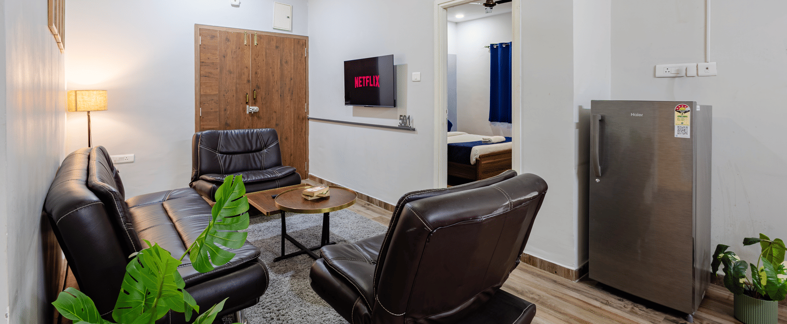 Separate living room of 4BHK featuring sofas with a centre table facing the wall-mounted TV and a doorway leading to an inner bedroom.