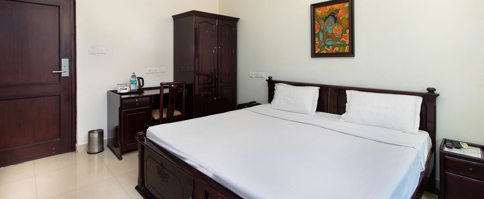 A room with a neatly arranged double bed, wooden furnishings, bedside tables, and a warmly lit lamp for a relaxing atmosphere at Sanctum Suites Indiranagar, Bangalore.