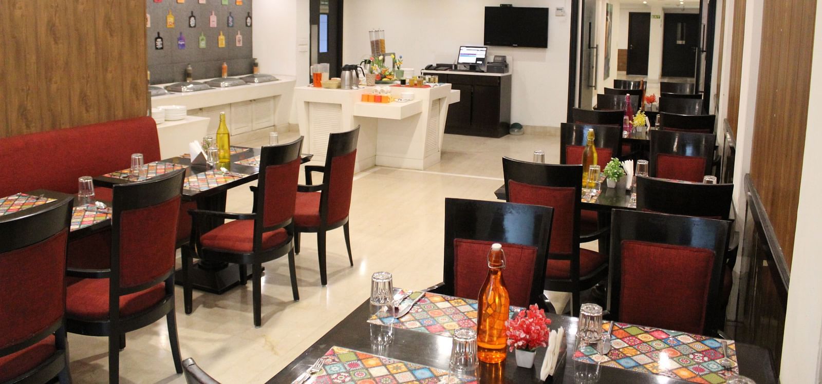 An image of a restaurant several sets of chairs and table where plates, cutlery, napkin, water bottles and other items are kept - Inde Hotels Vista Woods