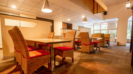 The Courtyard Restaurant at Featherlite Evoma Hotel with wooden dining tables, red cushioned chairs and warm pendant lighting overhead.