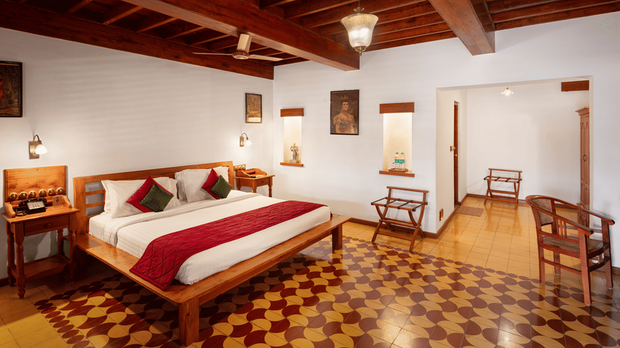 A bedroom at Chidambara Vilas - A Luxury Heritage Resort, with wooden flooring and ceiling, a large bed with spreads, and warm lighting.