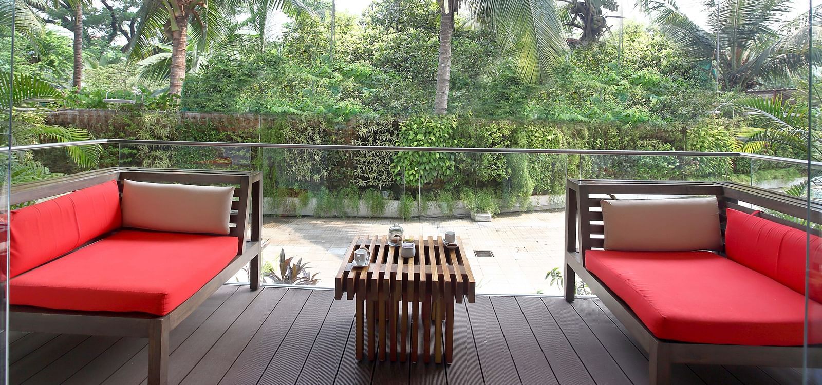 Image of two red sofas in the courtyard of the hotel with a wooden centre table and greenery all around. | Mirage Hotel