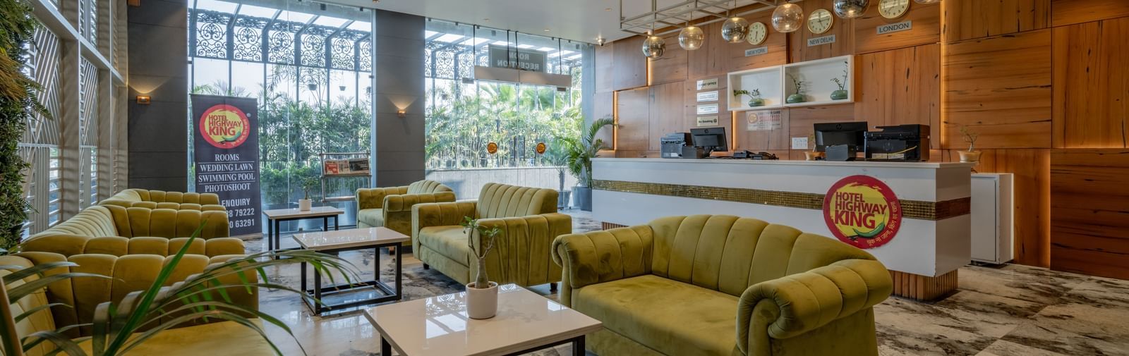 Lounge and reception area at Hotel Highway King, Bagru, featuring sofas, tables, large windows, and wooden paneled walls.