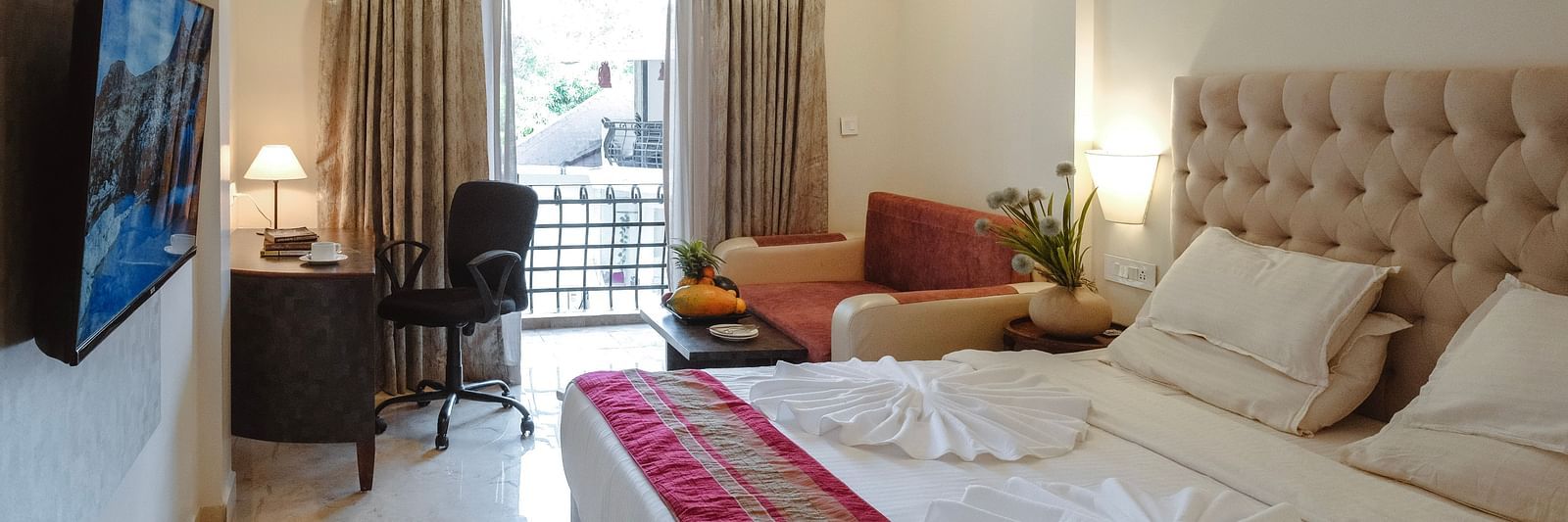 A spacious bedroom featuring a bed, a large TV, and a balcony with natural light – The Verda de Miranda Resort.
