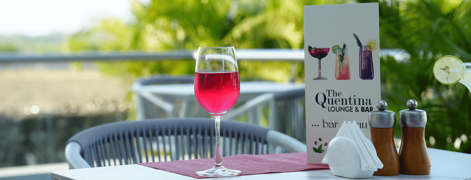 Close-up of a red cocktail displayed on an outdoor table from The Quentina Bar with greenery behind - Grande Bay Resort & Spa, Mamallapuram