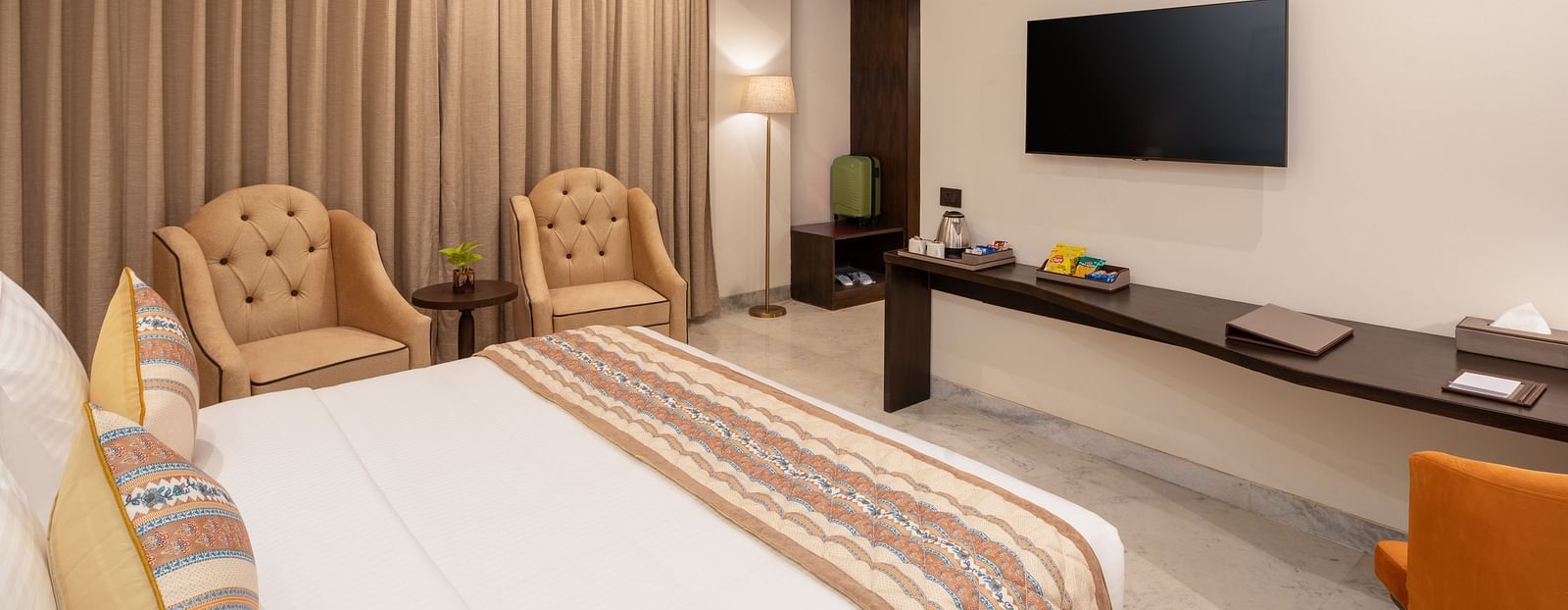 An image of a bedroom with double size, a photo frame hanged on the wall, two  chairs at one corner and opposite the bed there is a flat TV screen -  Brij Eternity, Vrindavan