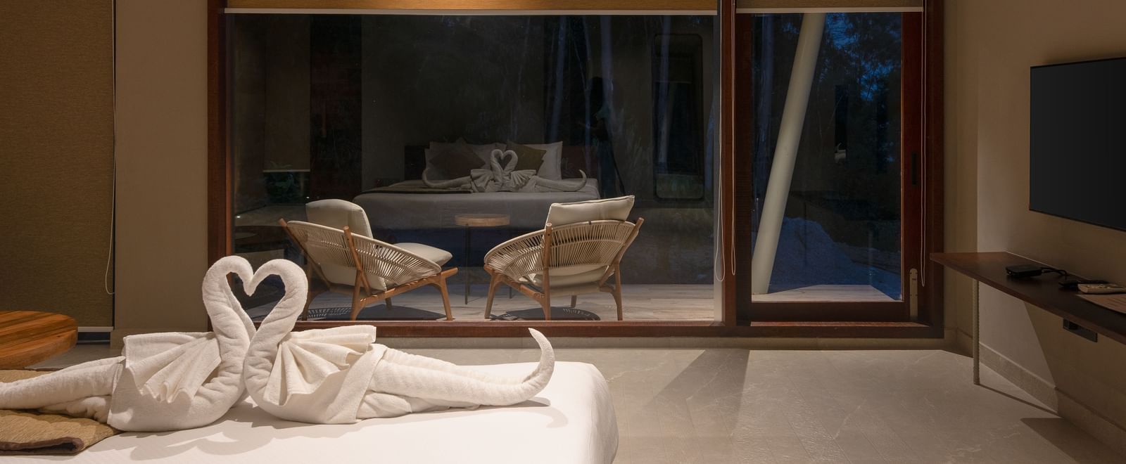 A hotel room featuring a bed with swan towel art, a large window, and modern furnishings | Gaia Room | RD's Nature Retreat, Bangalore