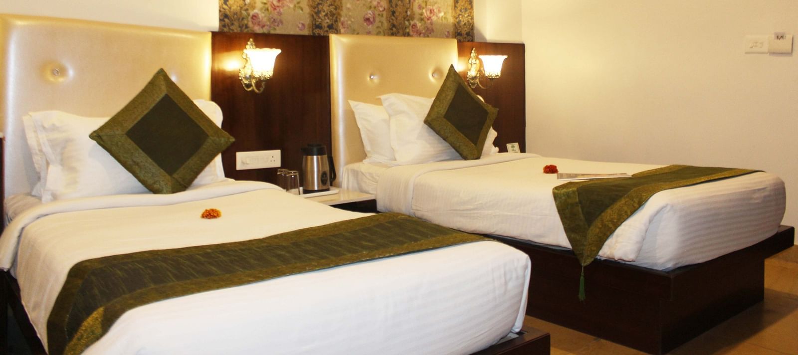 A hotel room with two beds, green runners, floral wallpaper and a wooden headboard - TGI Apple Inn, Jaipur 