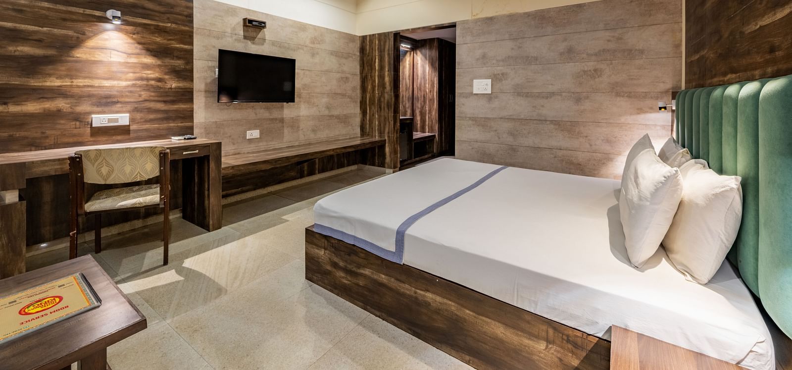 Extended view of the Maharaja Deluxe Room at Hotel Highway King, Behror, furnished with a double bed, wall-mounted TV, air-conditioning, a work desk and wardrobe.