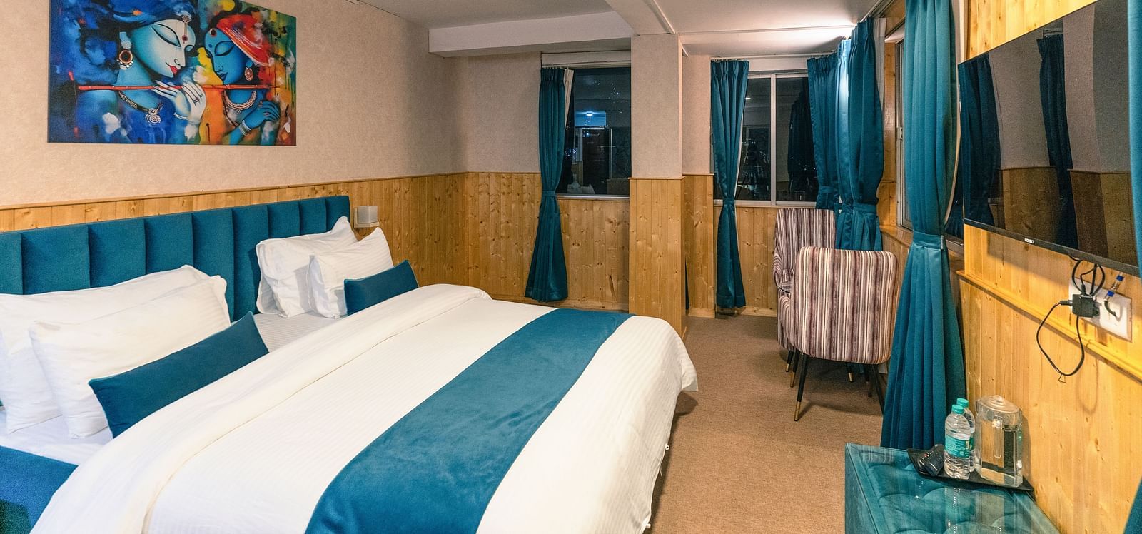 Deluxe Room with a king size bed, inviting ambiance, wooden bedside table, and a wall mounted television at Avianna Seven Seas, Darjeeling.
