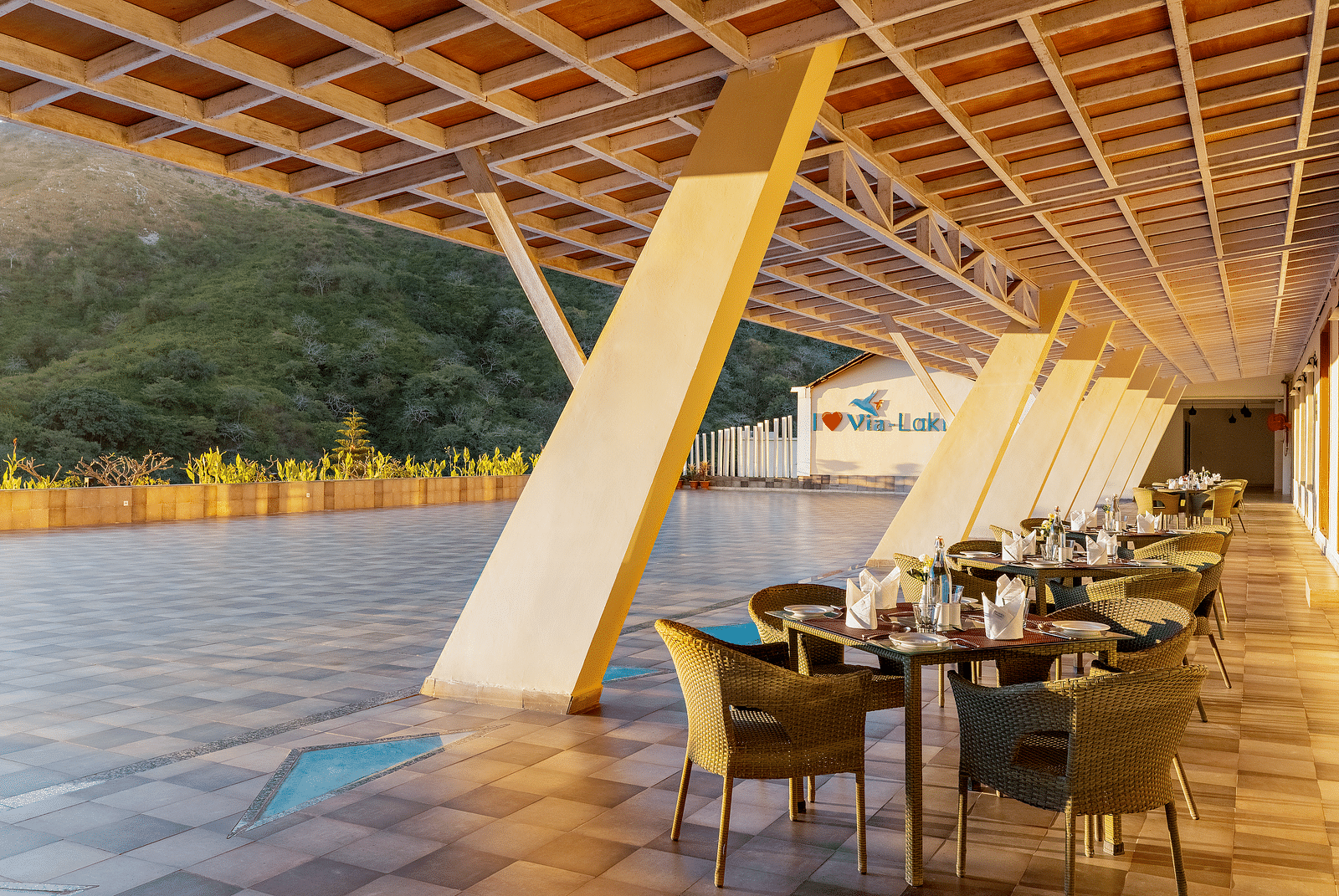 Outdoor dining area with tables, chairs, and a unique sloped roof - Via Lakhela Resort & Spa