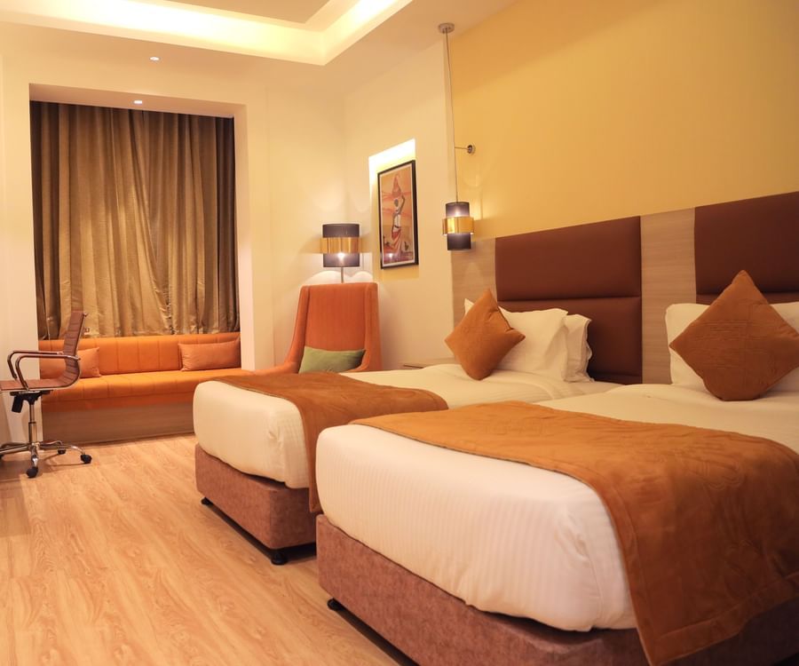 Warmly lit room featuring twin beds with brown throws, work desk, sofa seating, wooden flooring, and warm contemporary lighting at Best Western, Vrindavan