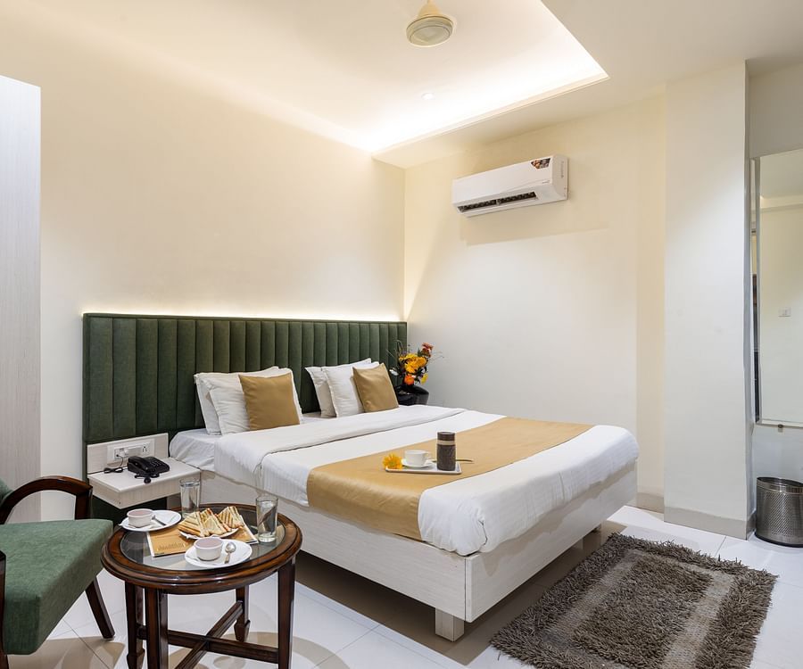 A room featuring a green sofa chair, a coffee table, a/c, wardrobe and neat bed - Hotel Meghdoot, Bhopal