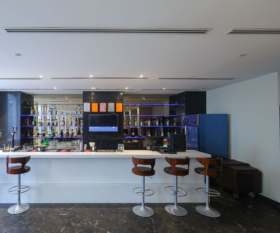 Bar counter with high chairs and shelves of bottles at Icon Premier Hotel by Bhagini, Devarabisanahalli