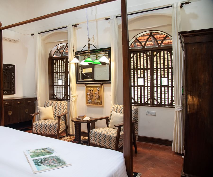 An image of a bedroom featuring a bed, a wardrobe, a work desk and chair, and two vintage styel windowds - Lamrin Ucassaim Hotel, Goa