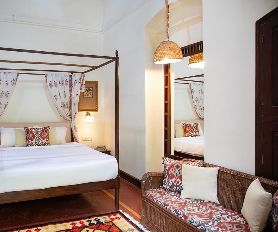 An image of a four poster bed with a sofa and bedside table on either side - Lamrin Ucassaim Hotel, Goa