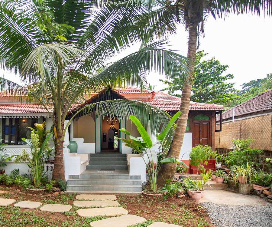 alt-text An image of a cottage style bungalow at Lamrin Ucassaim Hotel, Goa which is surrounded by palm trees