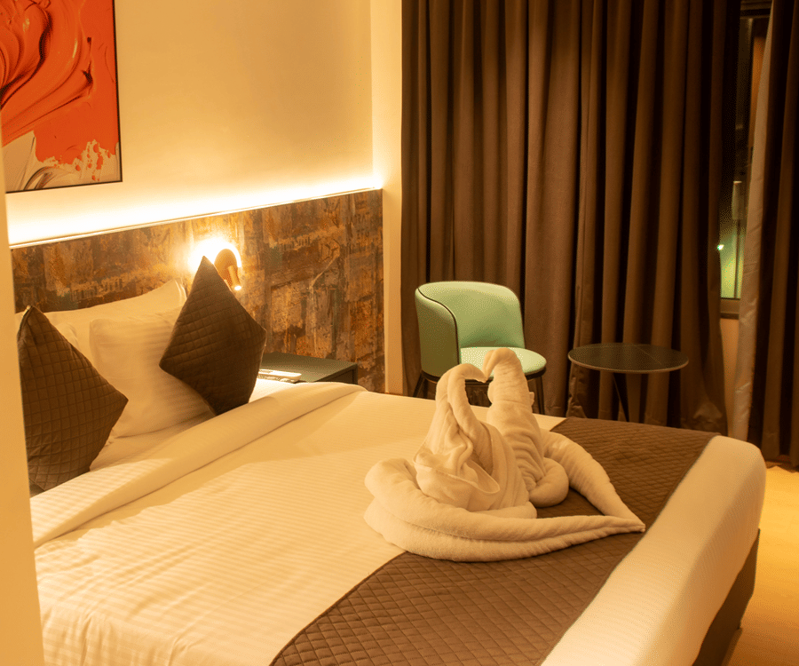 A bedroom with king size bed, bedside lamps, chair, table, wall art, and folded towel decor at Magnus Lxia Premier, Kalyani Nagar.