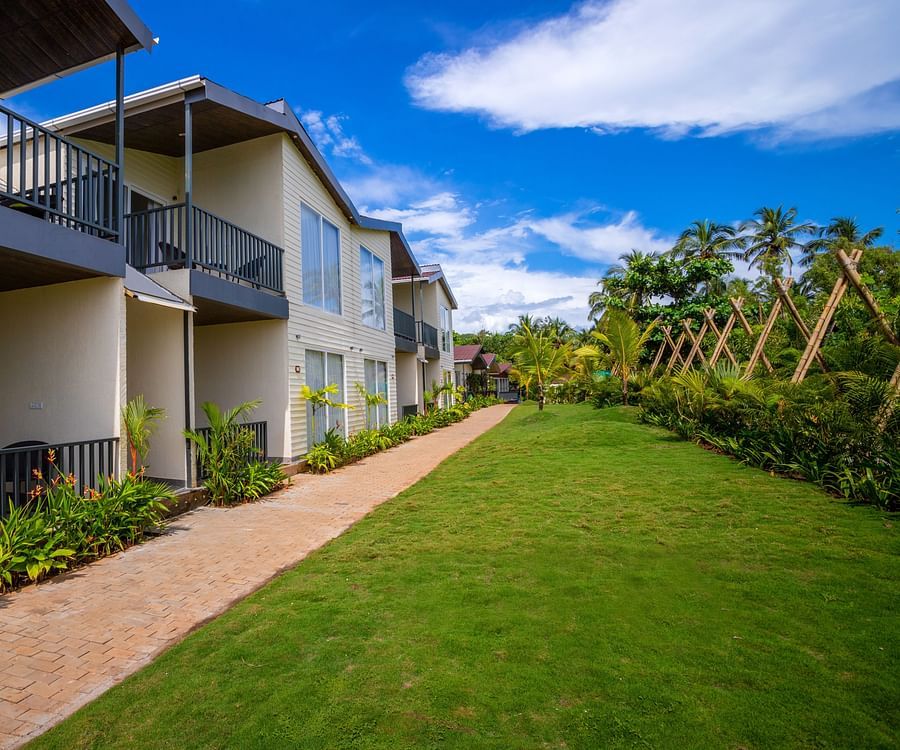 facade image of the sibaya beach resort, morjim beach with a serene green lawn in front of it