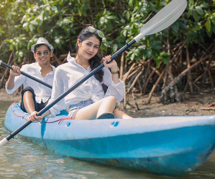 alt-text Two individuals, each in a kayak, paddling through calm river waters surrounded by dense mangroves, showing a peaceful and serene exploration setting.