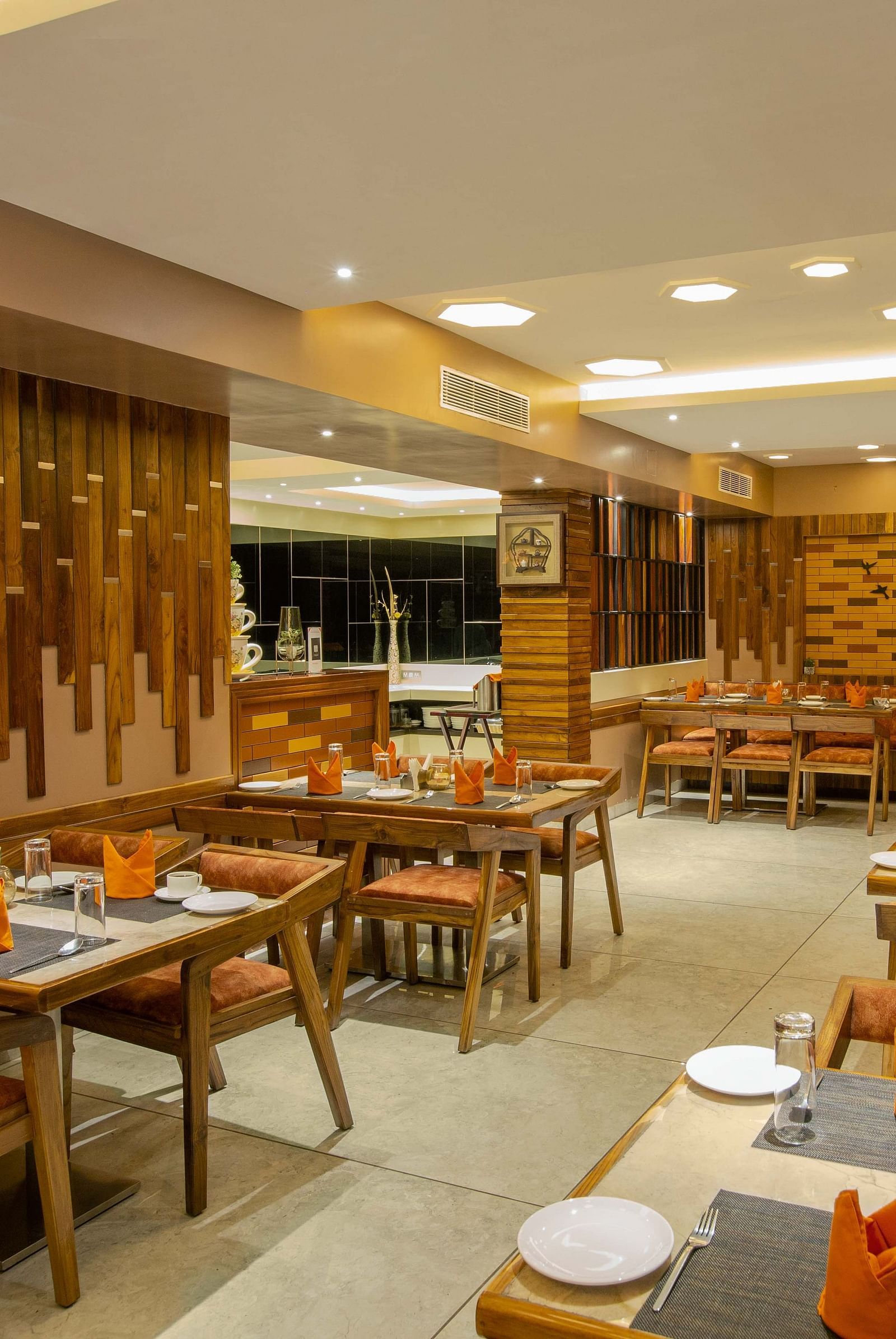 Image of Honeycomb Restaurant at Coral Reef Hotel & Spa in Port Blair showing dining setting of 4 chairs at each table and cutlery organised