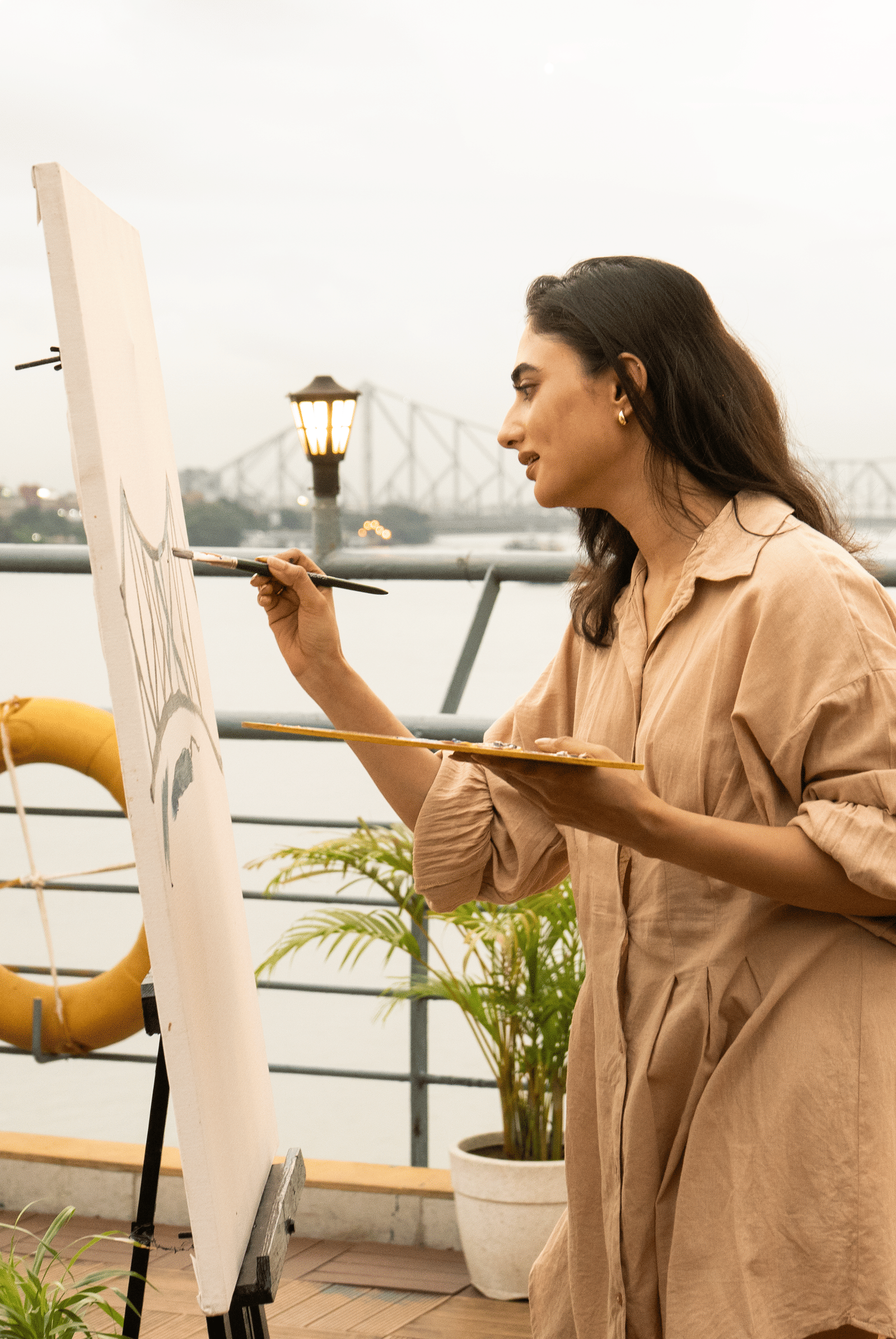 Woman painting on an easel on the deck of Polo Floatel Kolkata with the Howrah Bridge in the distance.