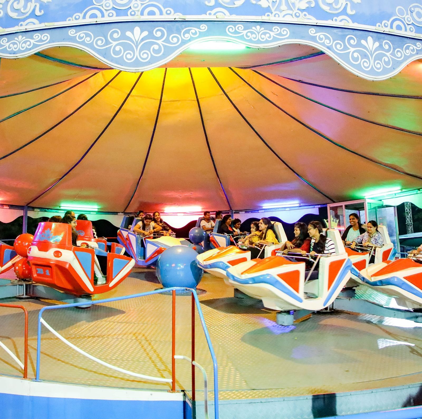 Visitors enjoy a colorful Break Dance ride under a canopy at Ramoji Film City, with vibrant lights enhancing the atmosphere.