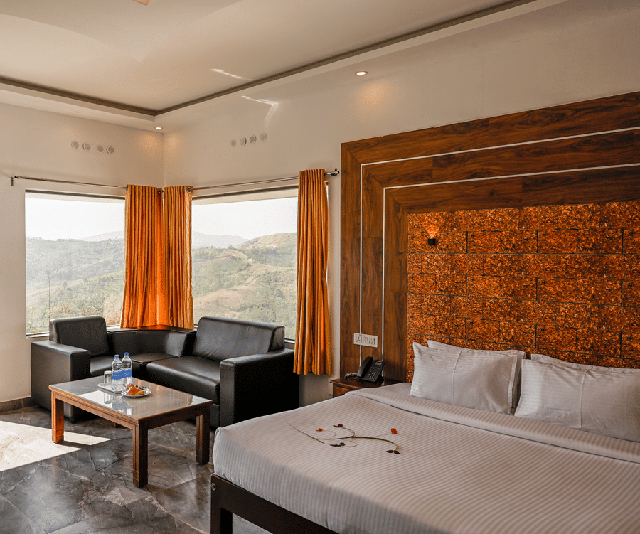 A hotel room featuring a bed with white linens, a black leather sofa, and large windows overlooking hills | Abad Silvermist, Vagamon