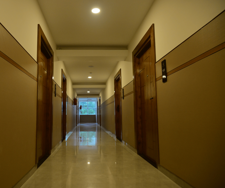  Well-lit hotel corridor at Bhavanis Vista By Icon Hosur with warm-toned walls, wooden room doors, and polished flooring