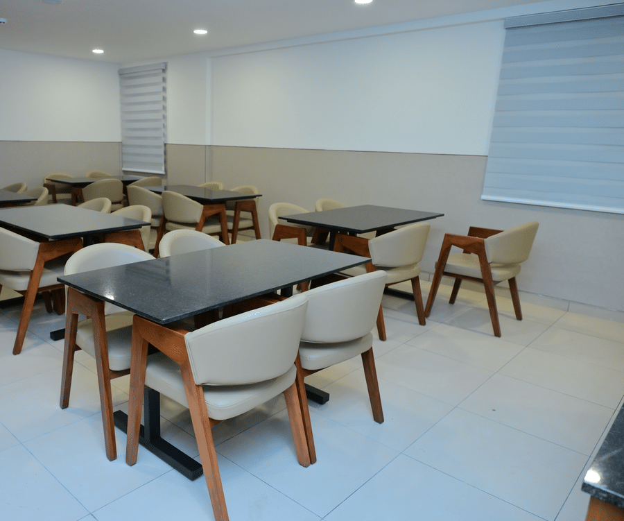 Modern restaurant interior at Bhavanis Vista By Icon Hosur with wooden dining chairs, dark-topped tables, and neutral-toned walls.