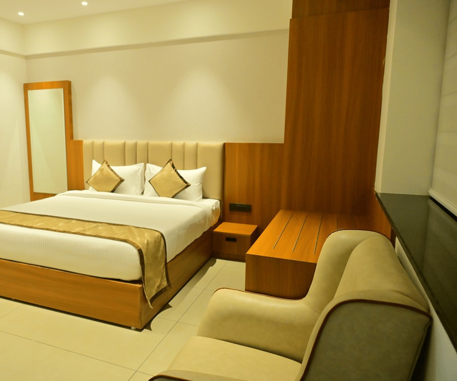 Suite bedroom at Bhavanis Vista By Icon Hosur with a king bed, wooden headboard panel, and a sofa seating area.