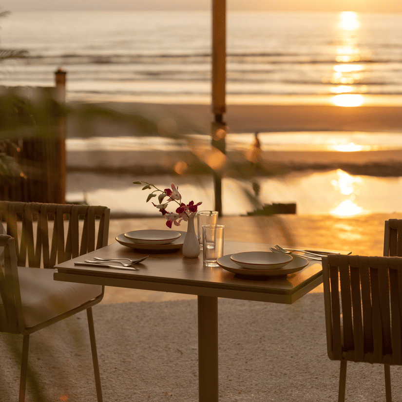 A close up shot of a table with two chairs at saz on the beach restaurant during sunset with sun rays reflecting on the sea waves in the background