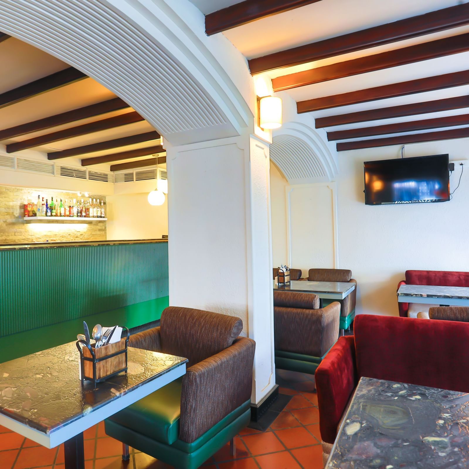 A cafe interior at Shilton International, Kochi, with tables, chairs, and booths, featuring a counter with shelves and a television.