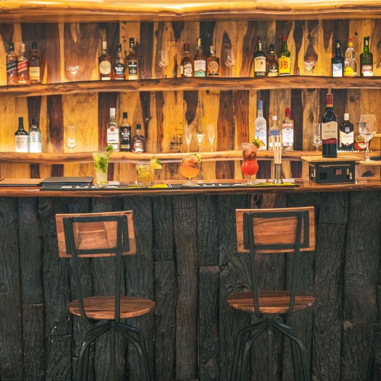 Bar counter with various alcohol bottles displayed and chairs placed in front of the counter