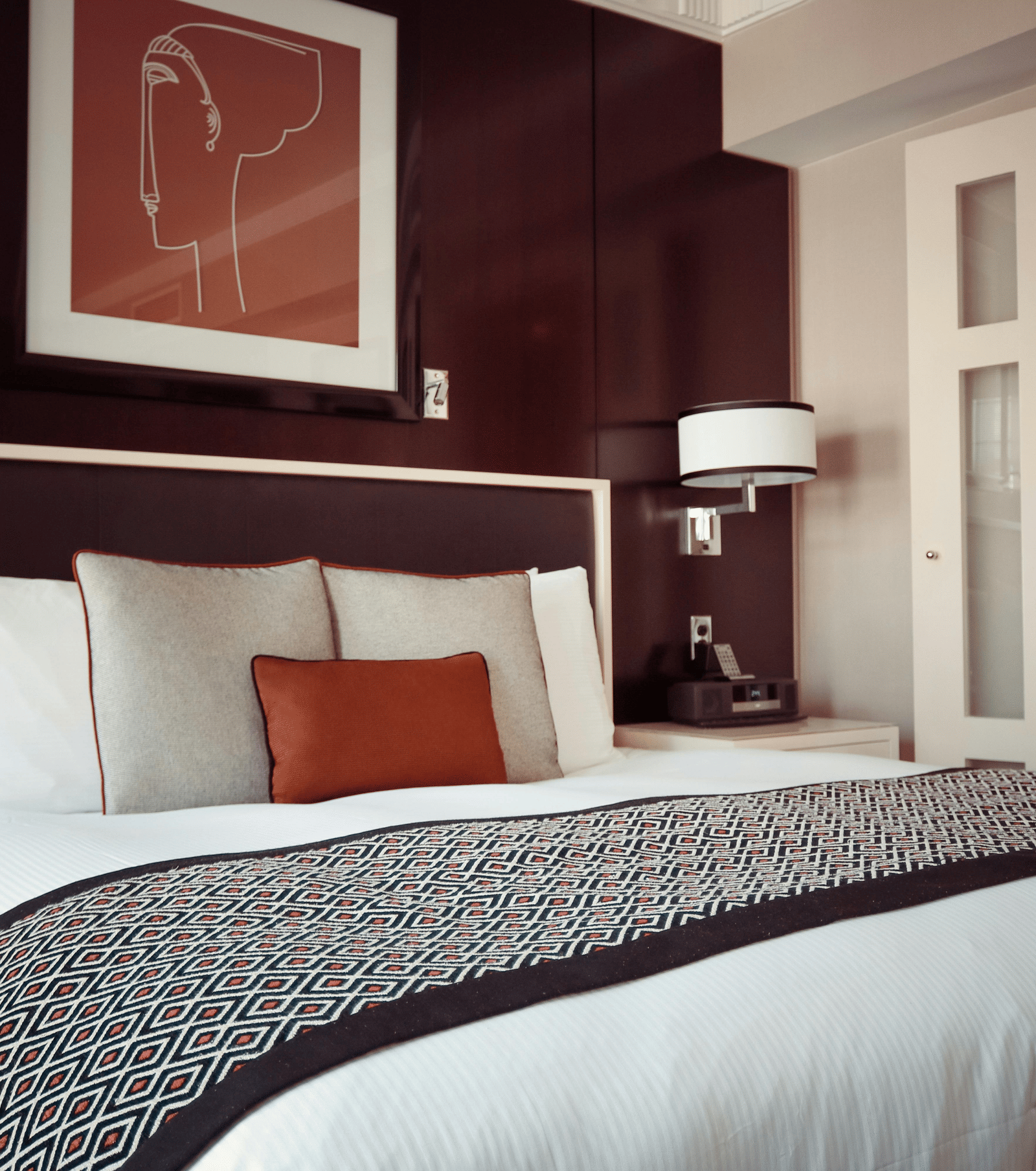 A luxurious hotel bedroom with a large bed, dark wood panelled walls, and an adjoining en-suite bathroom visible through glass doors.