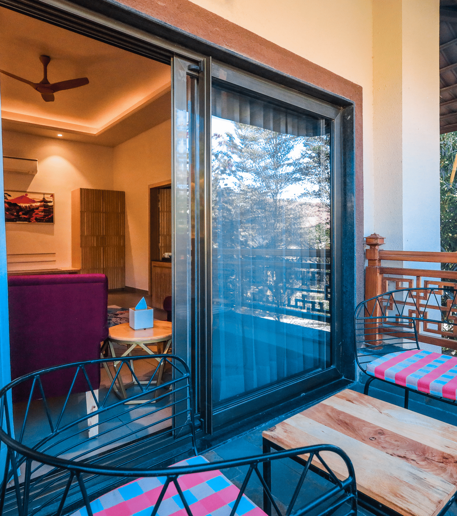 A balcony with chairs, a table and a sliding door leading to an indoor room at Ananta Spa & Resort, Jaipur.