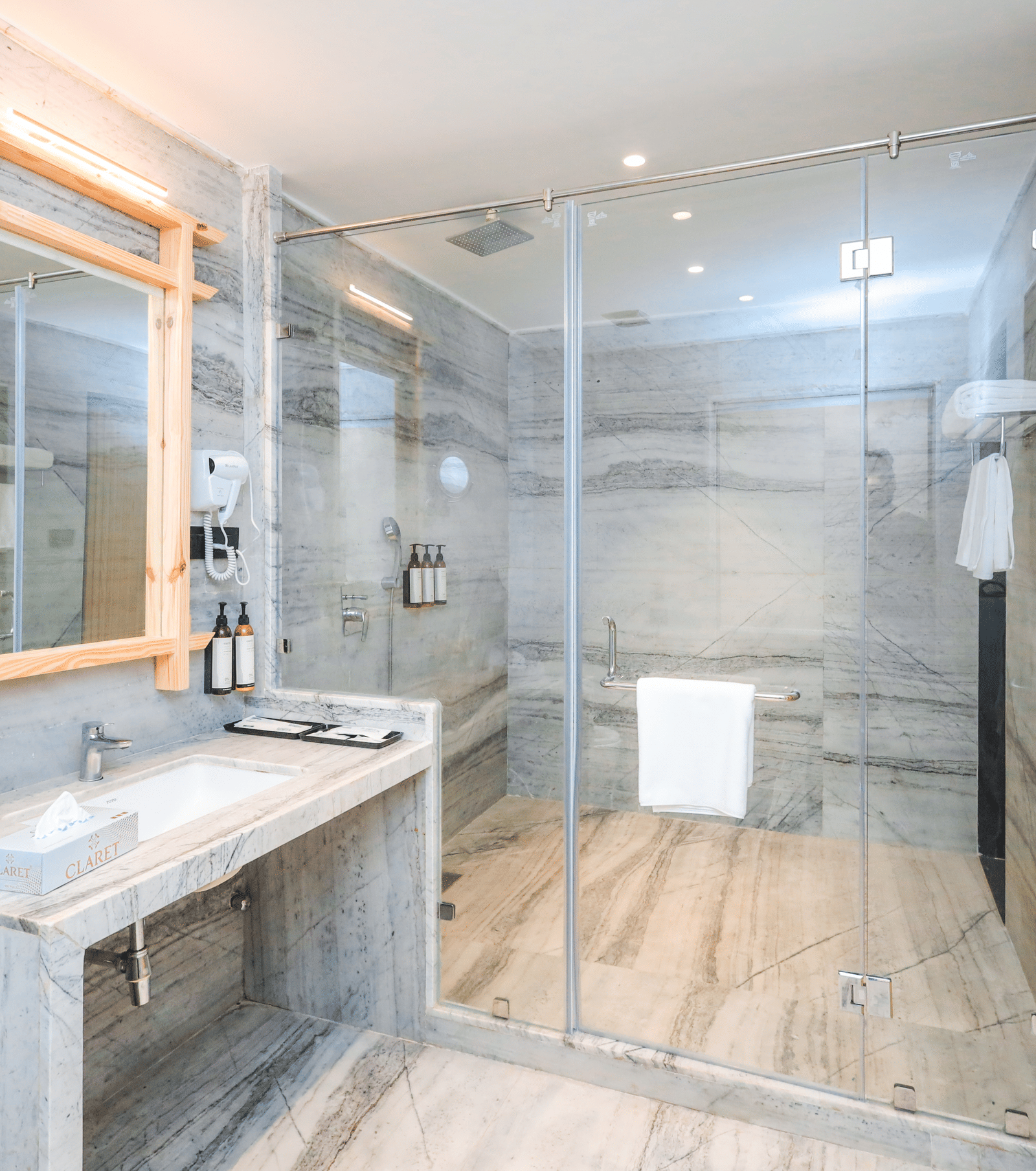 A washroom shows two basins with mirrors, a shower enclosure, a robe on a hook and toiletries on the counter at Ananta Spa & Resort, Jaipur.