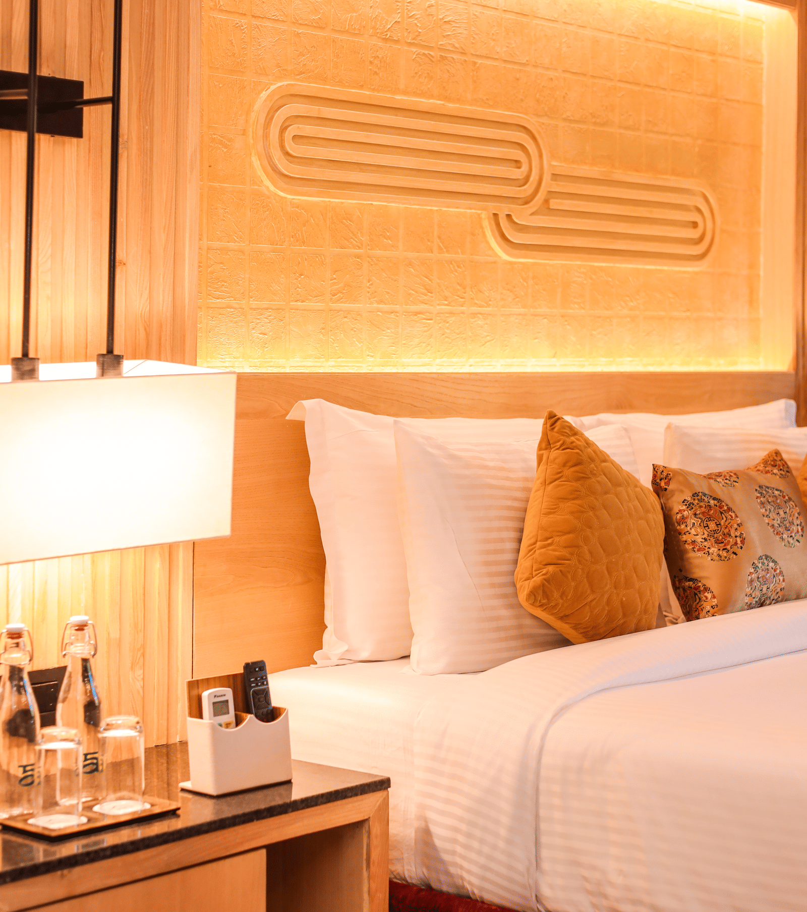 A room with a double bed, lamps, bottled water and side table viewed from one side at Ananta Spa & Resort, Jaipur.