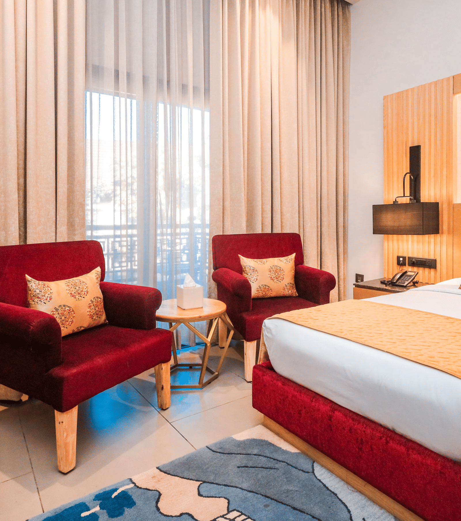 A room with a double bed, two chairs, curtains and lamps arranged around a central space at Ananta Spa & Resort, Jaipur.