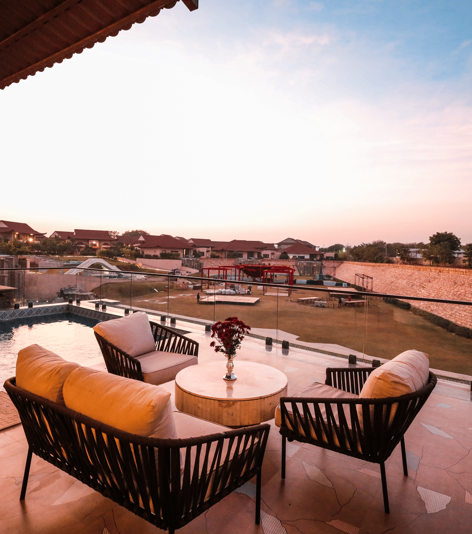 An outdoor space shows lounge chairs and tables beside a pool with landscape views in the distance at Ananta Spa & Resort, Jaipur.