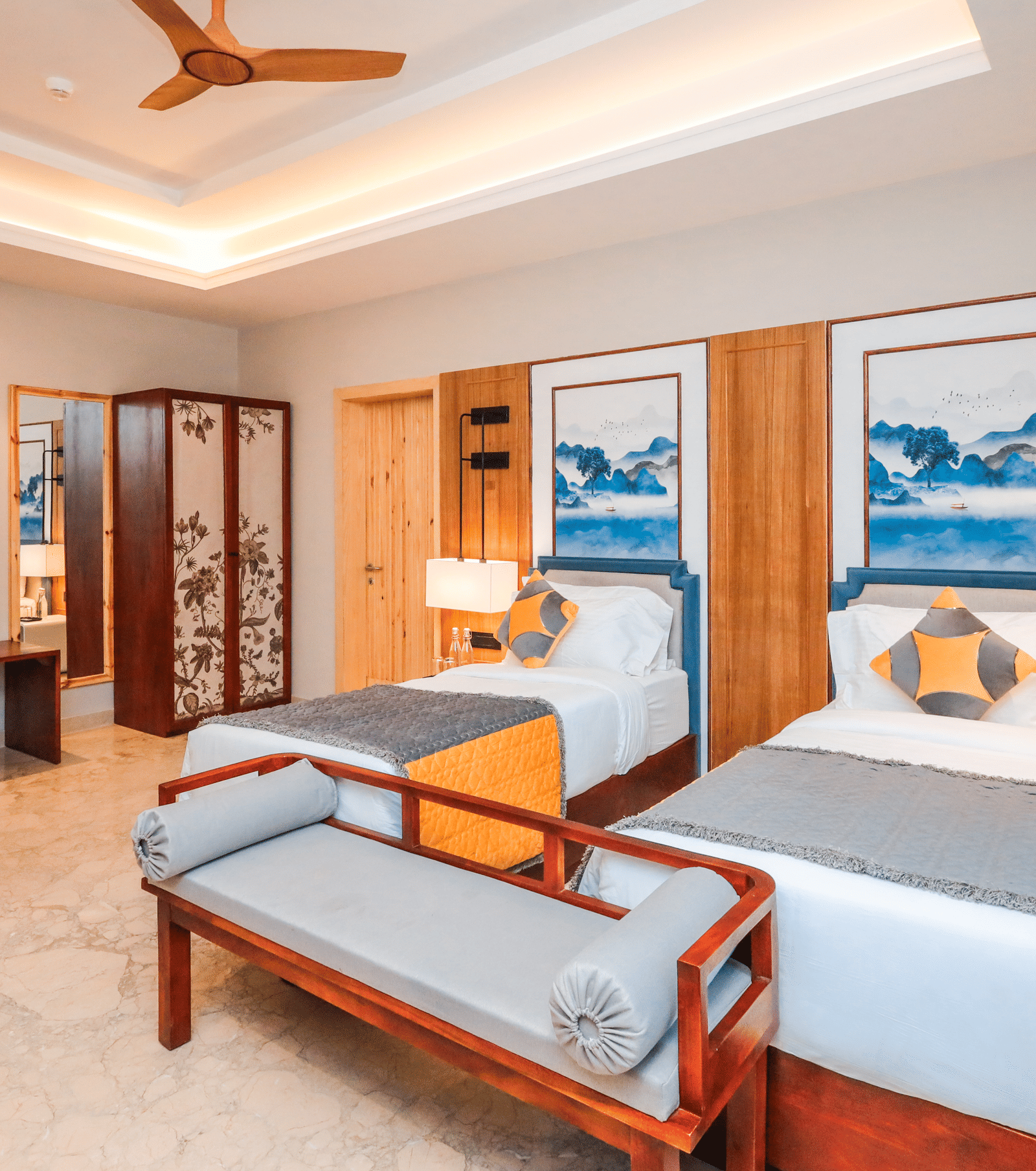 A room shows a bed with side tables, chairs with a table, storage units, artwork on the wall and a doorway at Ananta Spa & Resort, Jaipur.