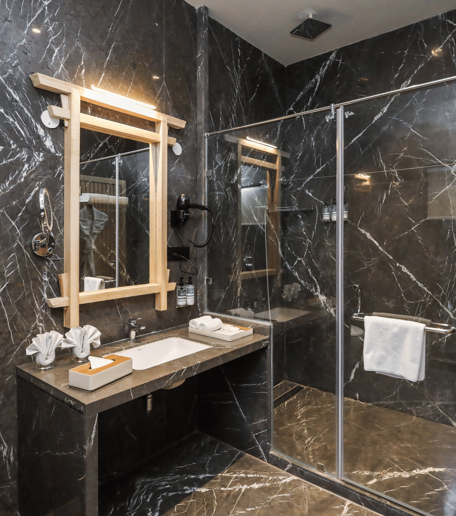 A washroom shows a basin with a mirror above it, a glass shower enclosure beside it and toiletries placed on the counter at Ananta Spa & Resort, Jaipur.