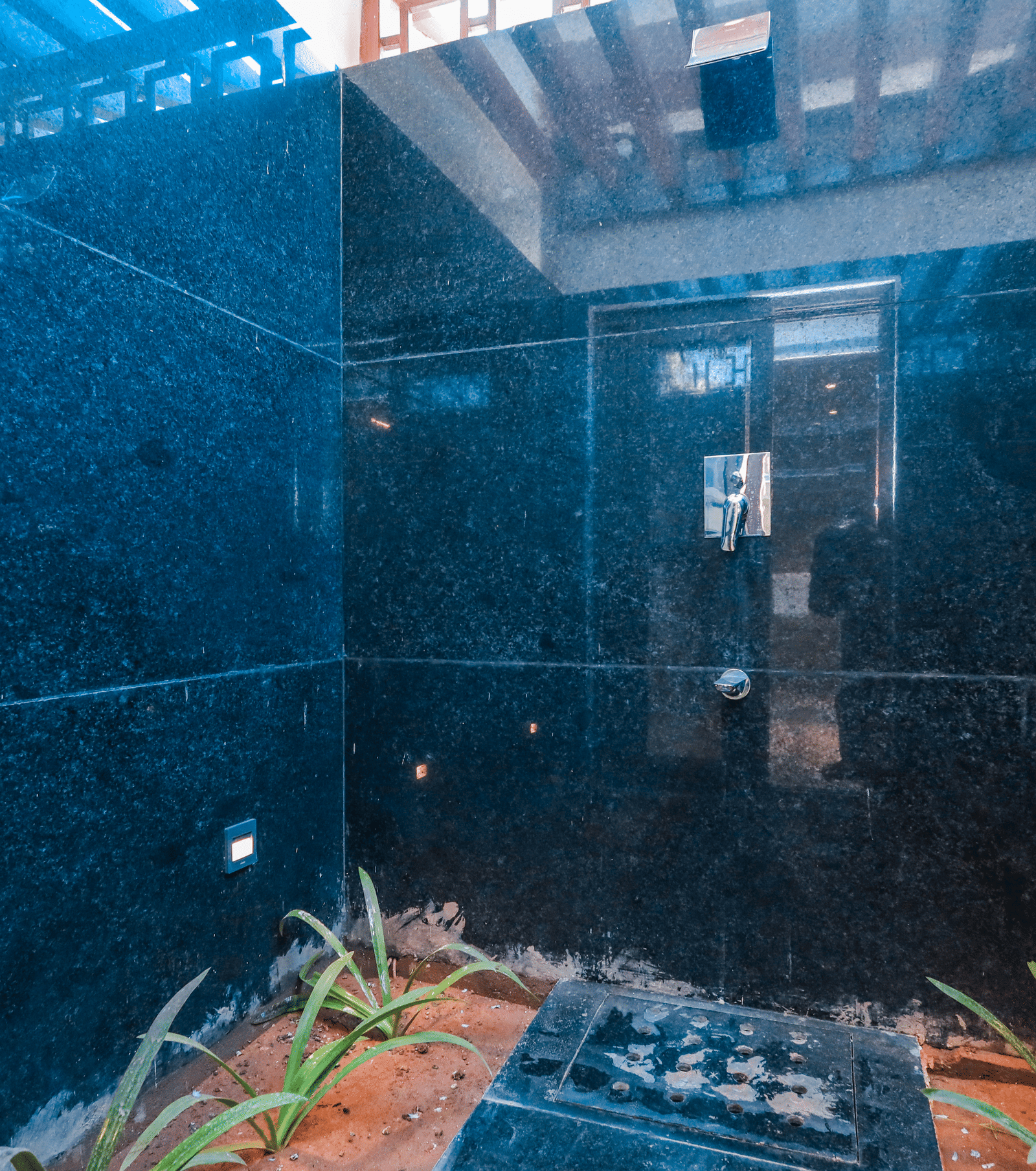 An outdoor space shows a high tiled wall with flowing water falling into a planted area at Ananta Spa & Resort, Jaipur.