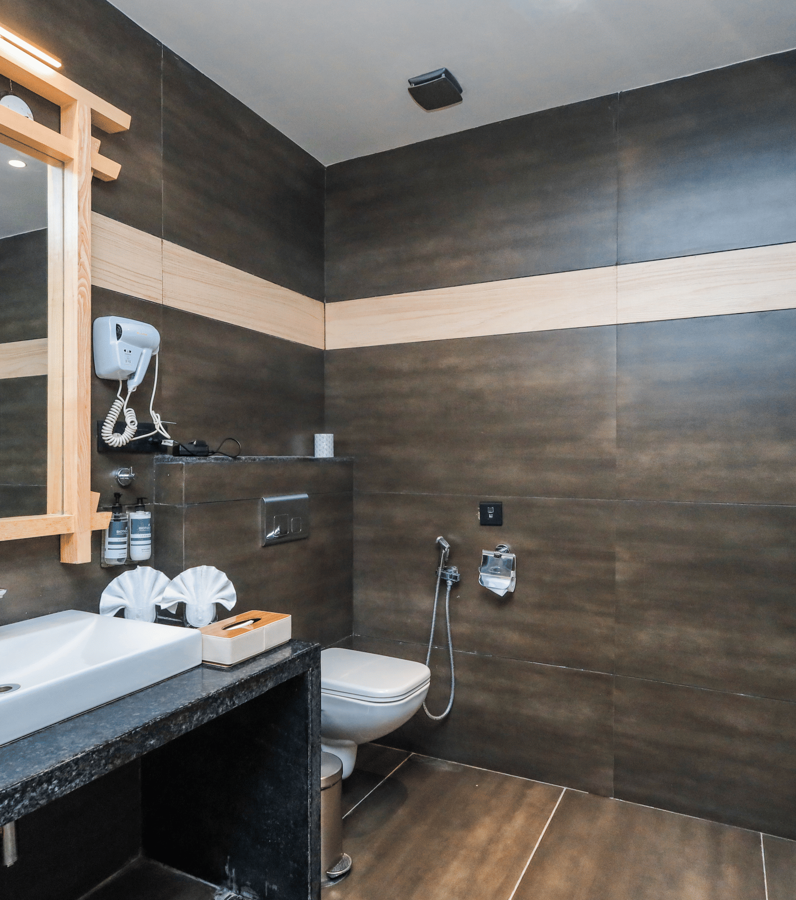 A bathroom with a sink, mirror, mounted hairdryer and shower enclosure at Ananta Spa & Resort, Jaipur.